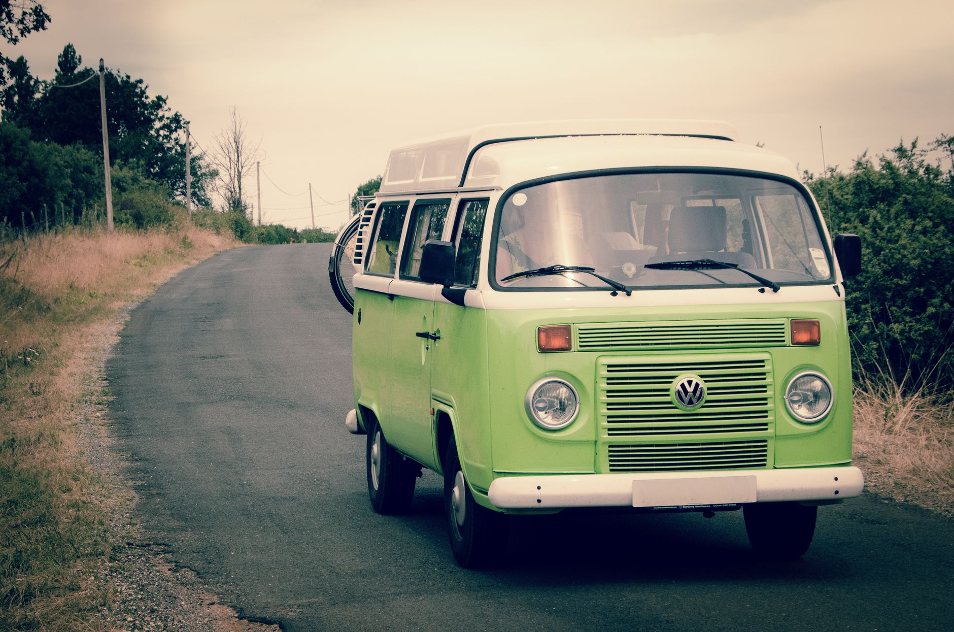 Kombi verde clássica rodando em uma estrada cercada de vegetação